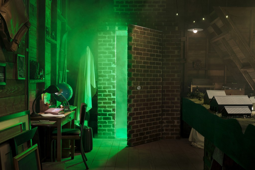 A brick wall appears to be opening up to another room with a green fog emanating from the opening.