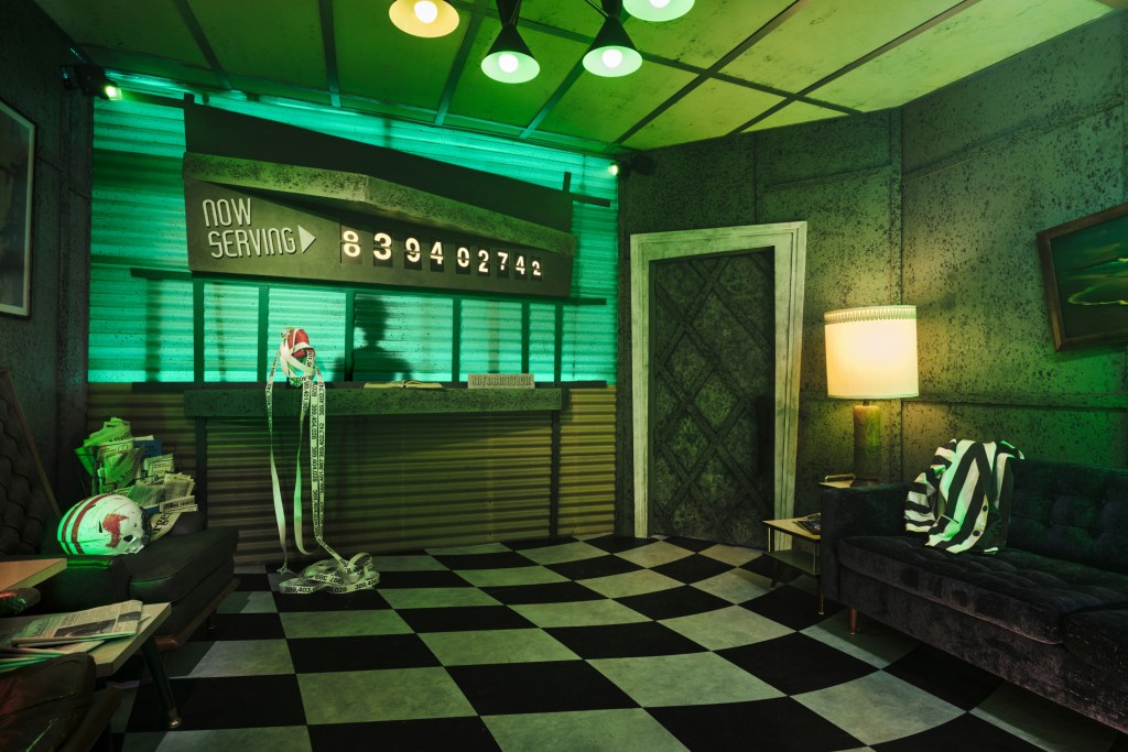 A waiting room scene with black and white tiled floor, and green hazy lighting throughout. A dark colored couch is on the right with a black and white striped jacket draped over it.