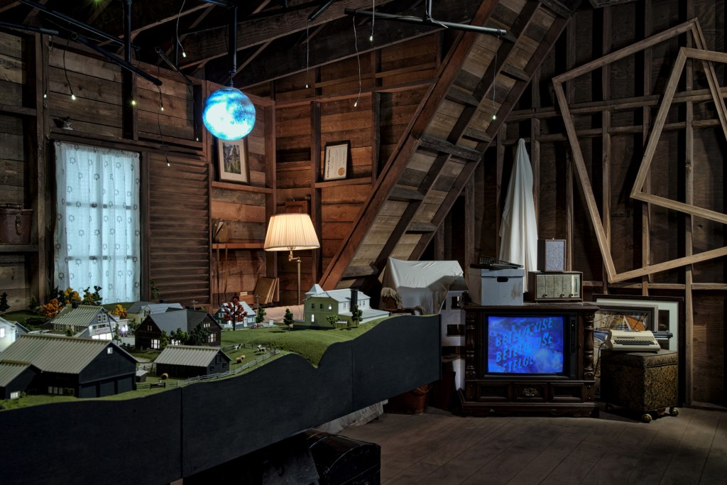 Attic wide shot showing a model town to the left and an old television with a hazy screen.