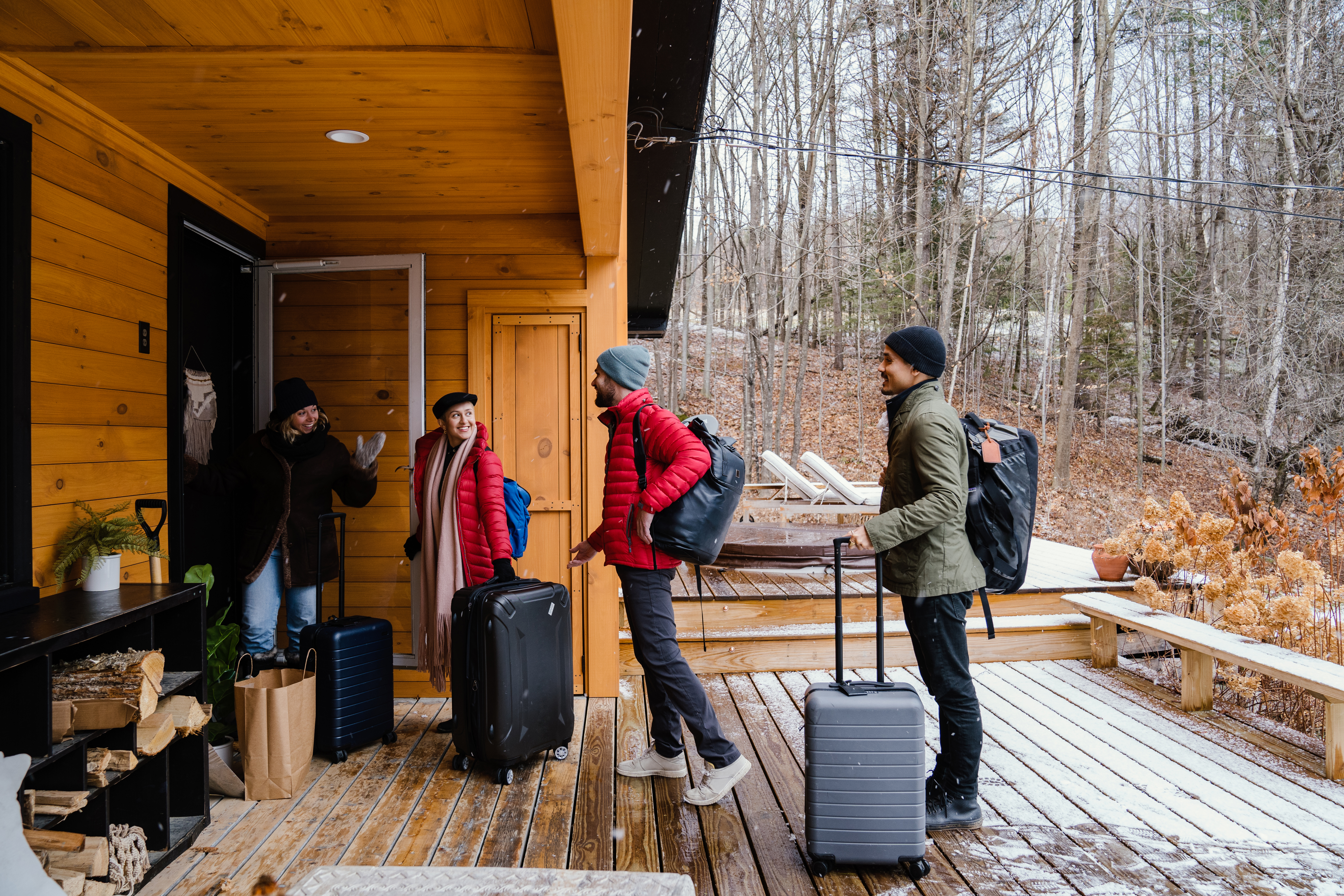 Four people with luggage on a snowy wooden cabin porch.