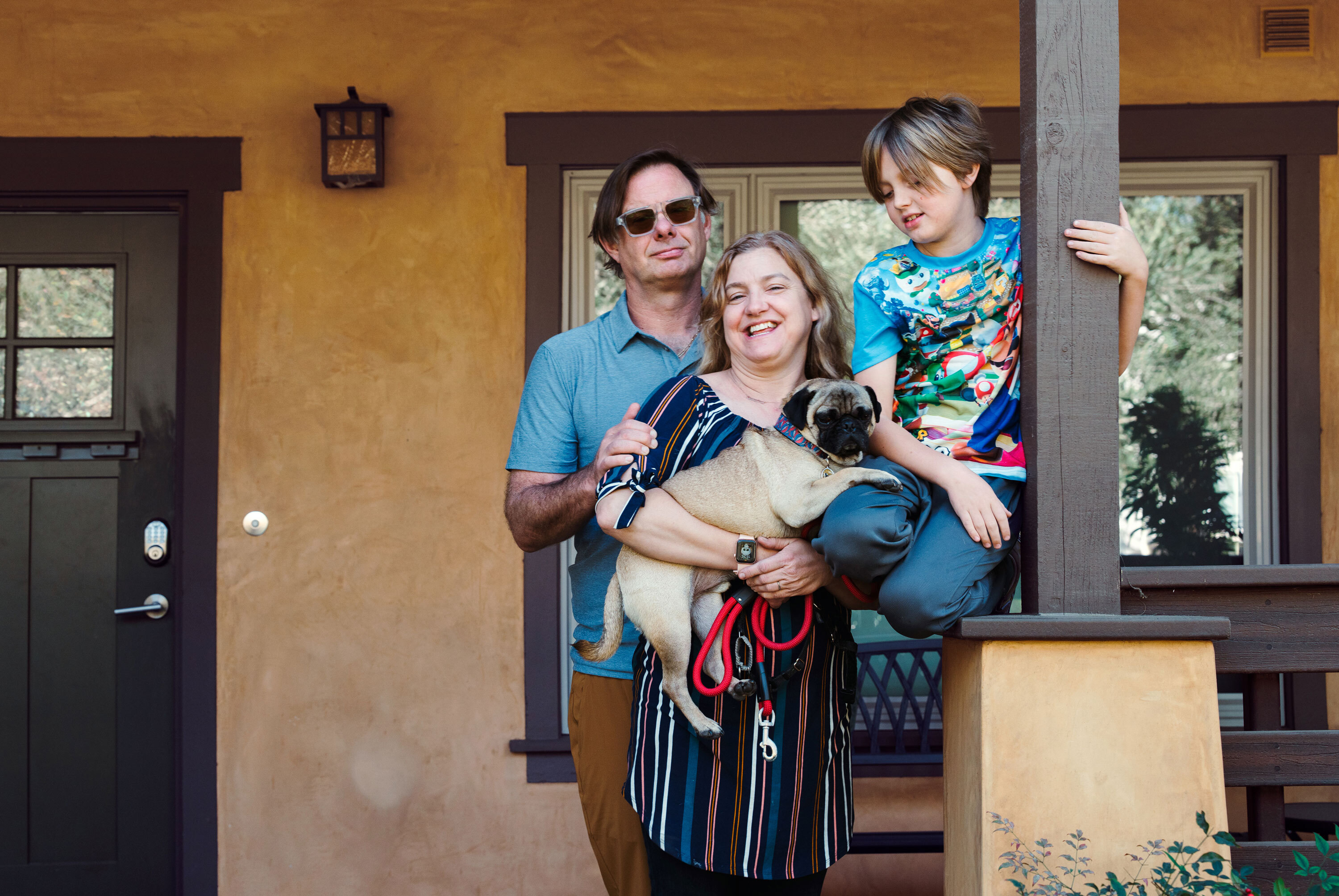 A man, woman, and their child stand in front of a beige house