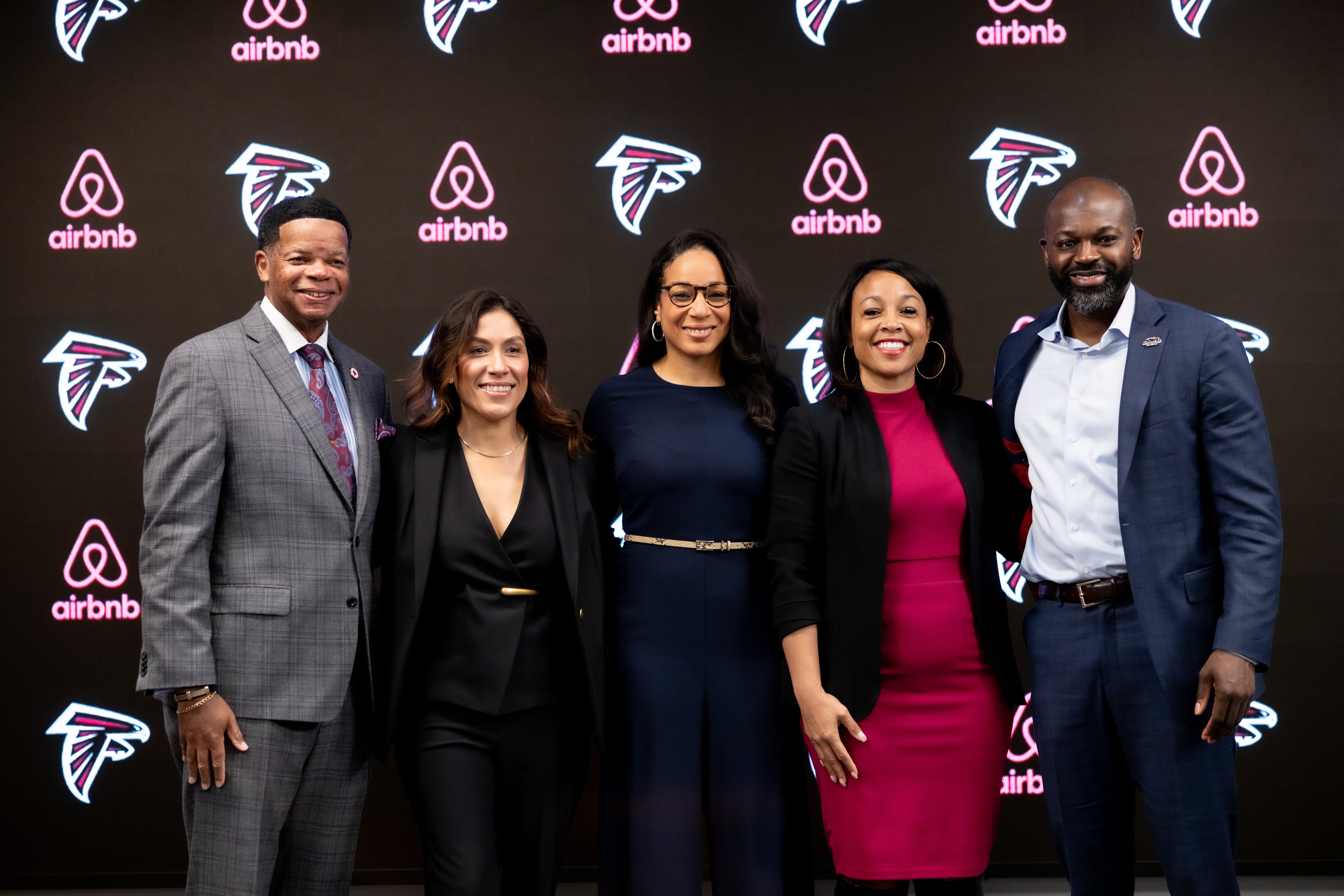 Five people stand in front of a black backdrop with repeating pink Airbnb logos and the Atlanta Falcons logo.