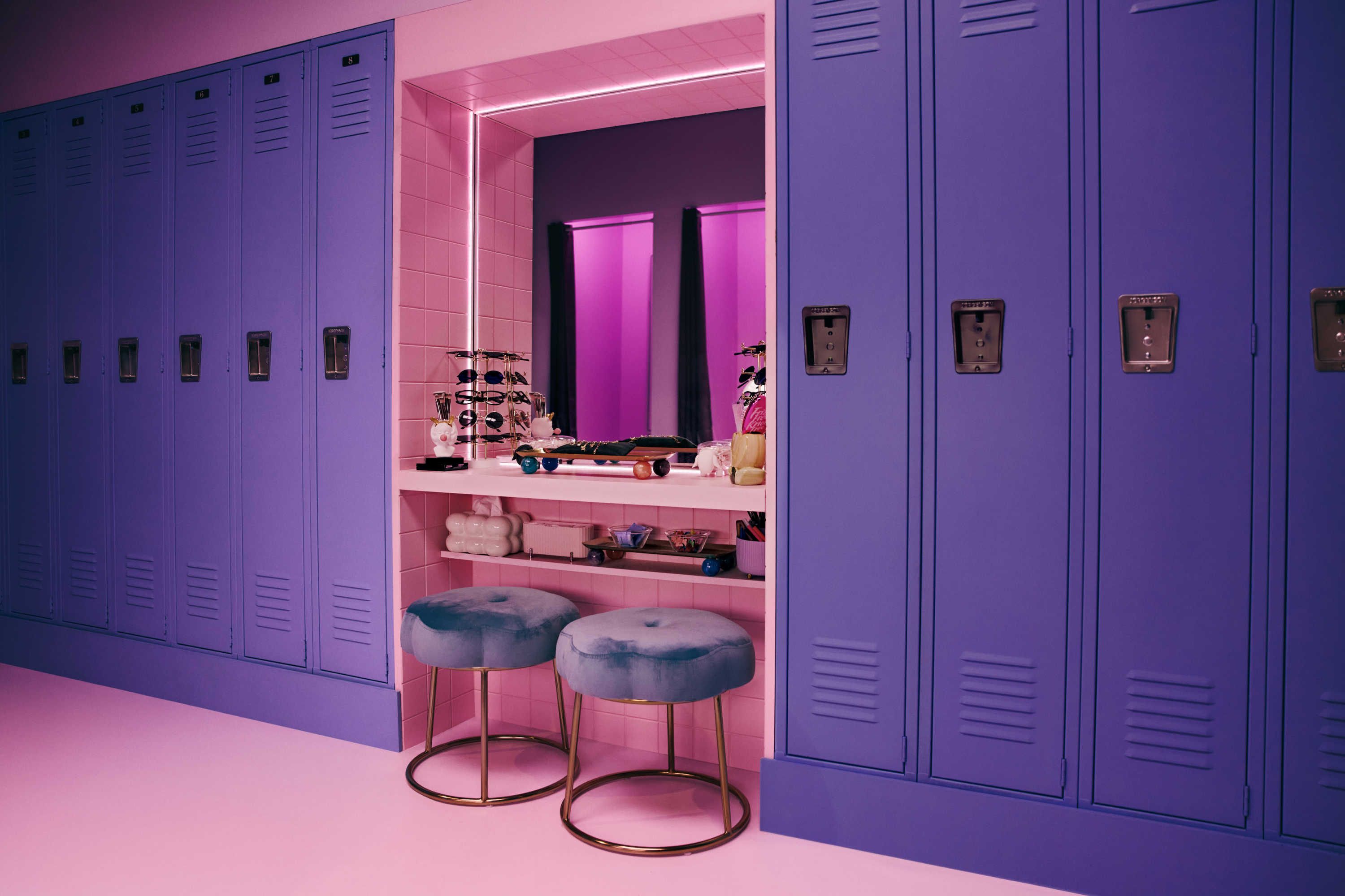 Colorful locker room with purple lockers, a vanity area, and two teal stools.