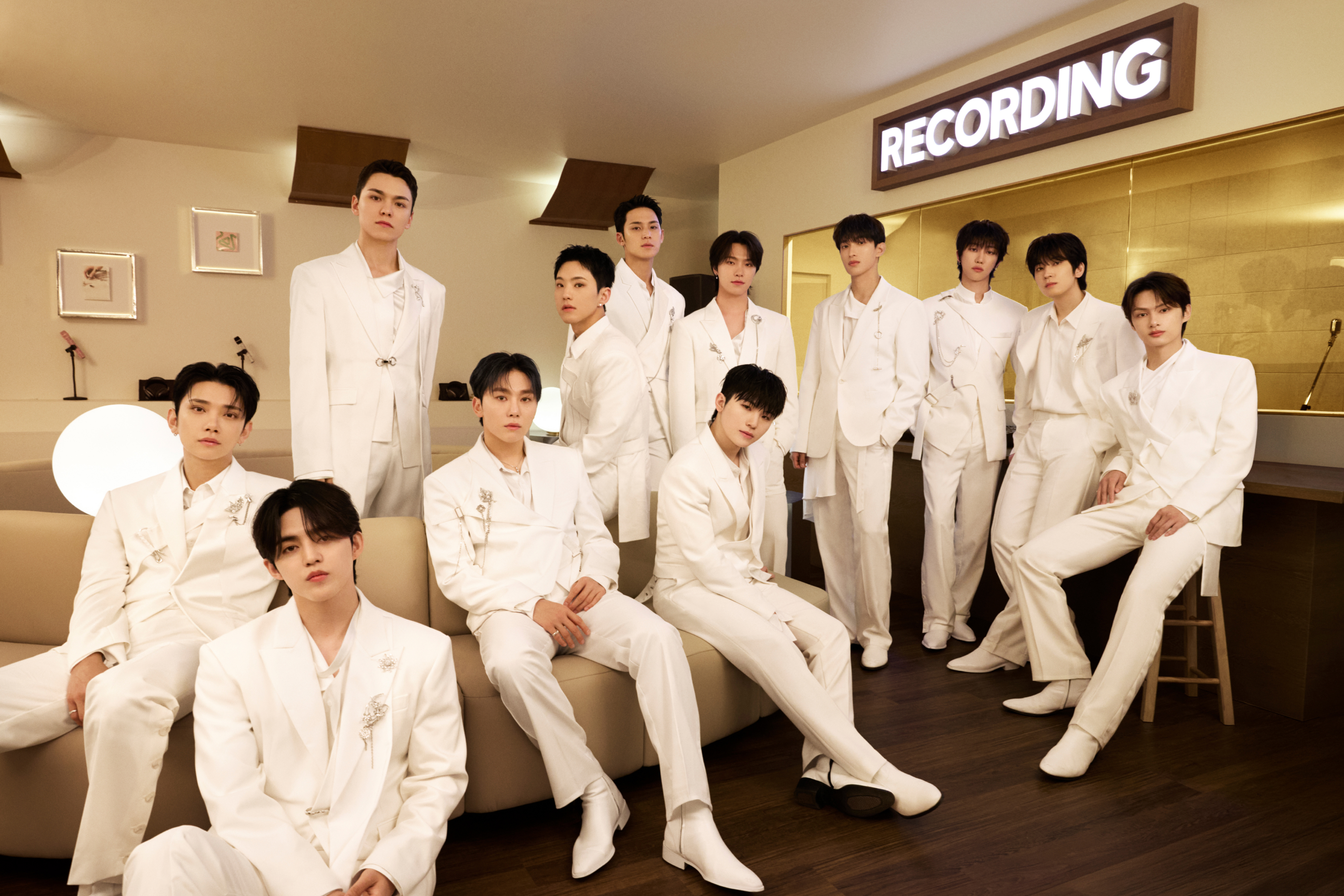 Men in white suits assembled in a recording studio, with a glowing 'Recording' sign in the background.