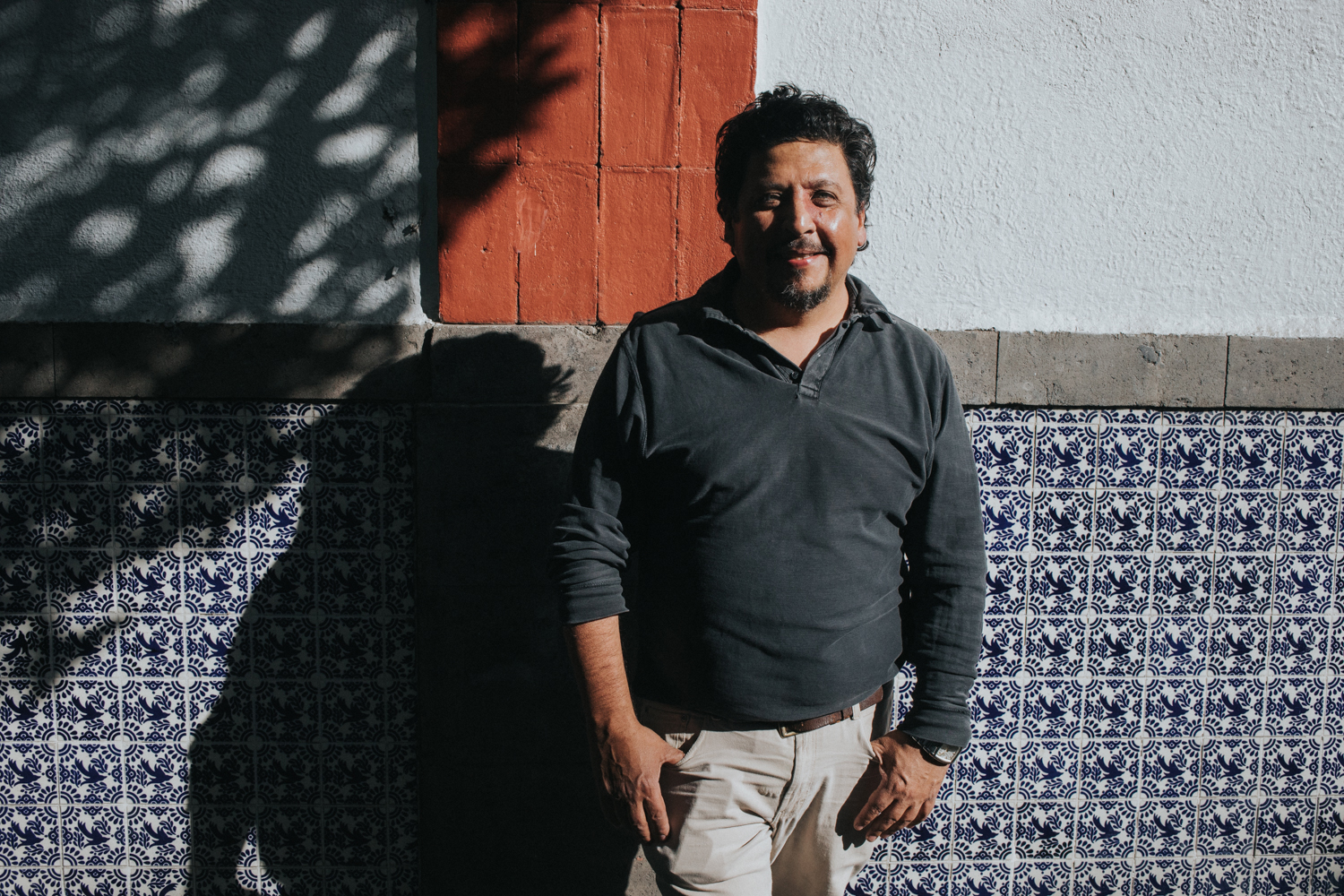 _P1A6008 Person standing against a wall with blue and white tiles and a red brick section.