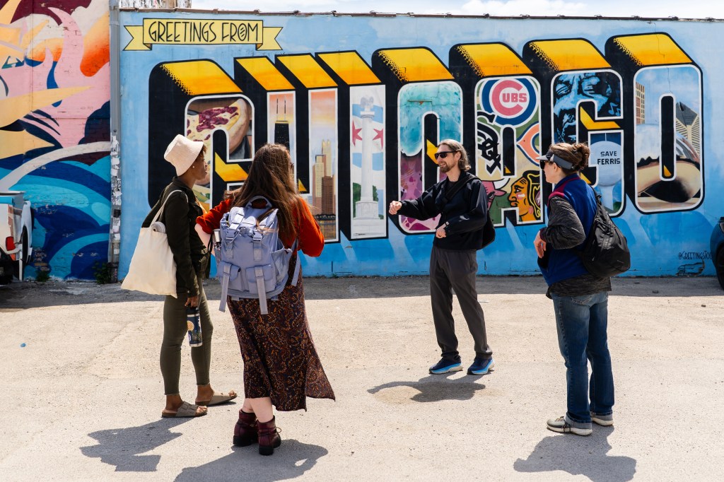 Group of people gathered near a vibrant street art mural with 'Chicago' written in bold, decorated letters and surrounding designs.