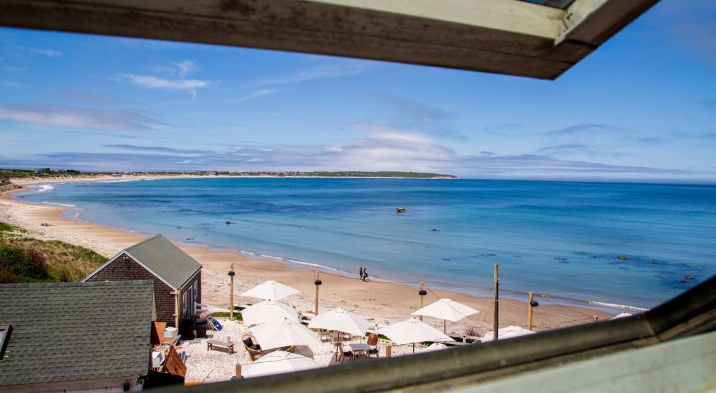 A serene beach scene with calm waves, sandy shoreline, and beachside umbrellas, framed by a window overlooking the coast.