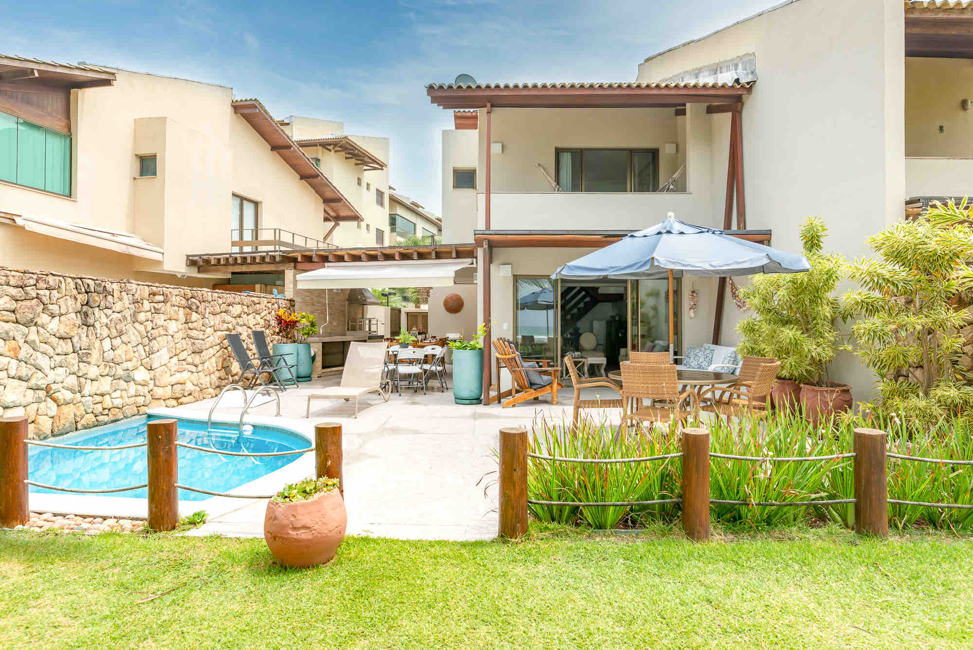 A bright modern villa features a private pool, shaded outdoor dining area, and lush greenery.