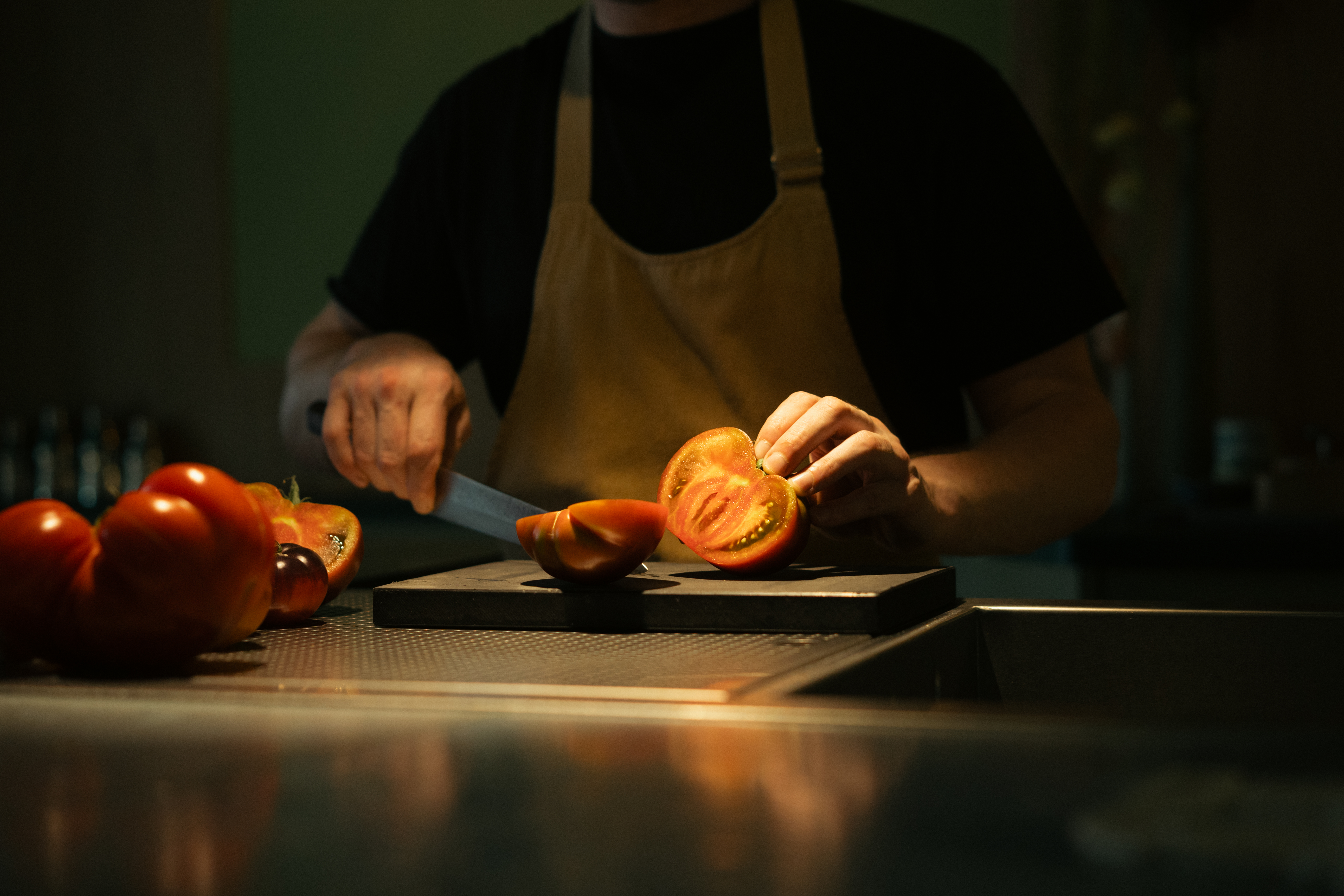 Someone is slicing a large tomato on a cutting board in a warmly lit kitchen.
