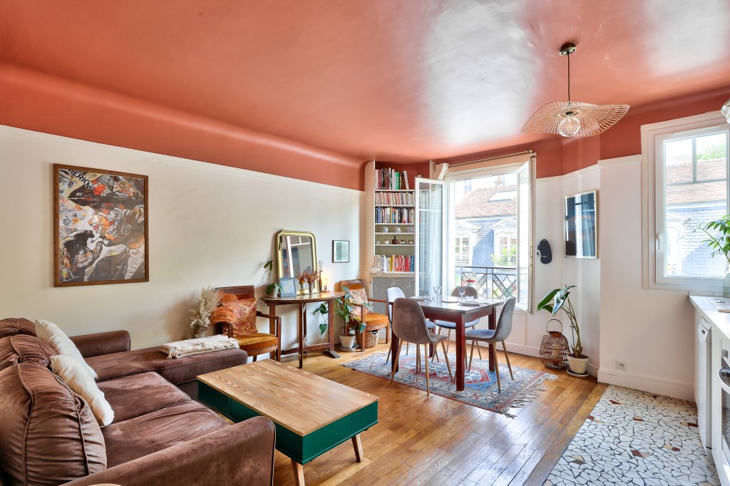 A charming living and dining area is enhanced by a warm terracotta ceiling, eclectic artwork, a plush sectional sofa, and a sunlit reading nook.