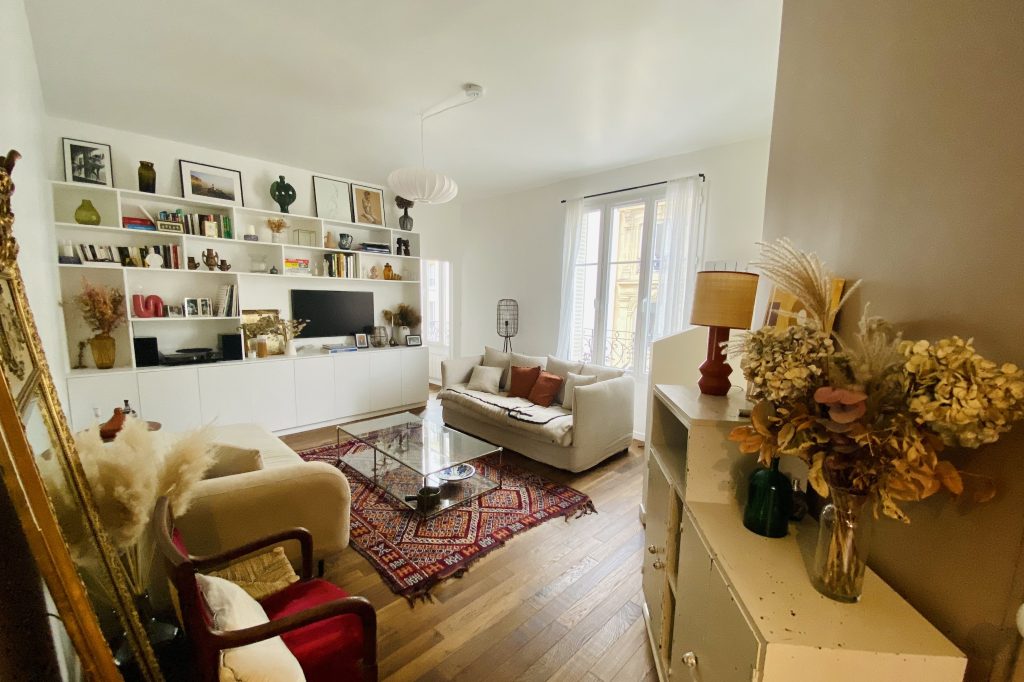 This inviting lounge is filled with natural light, open shelving, vintage accents, and a mix of cozy seating around a patterned rug.