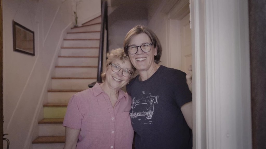 Two women hug at front door of home.