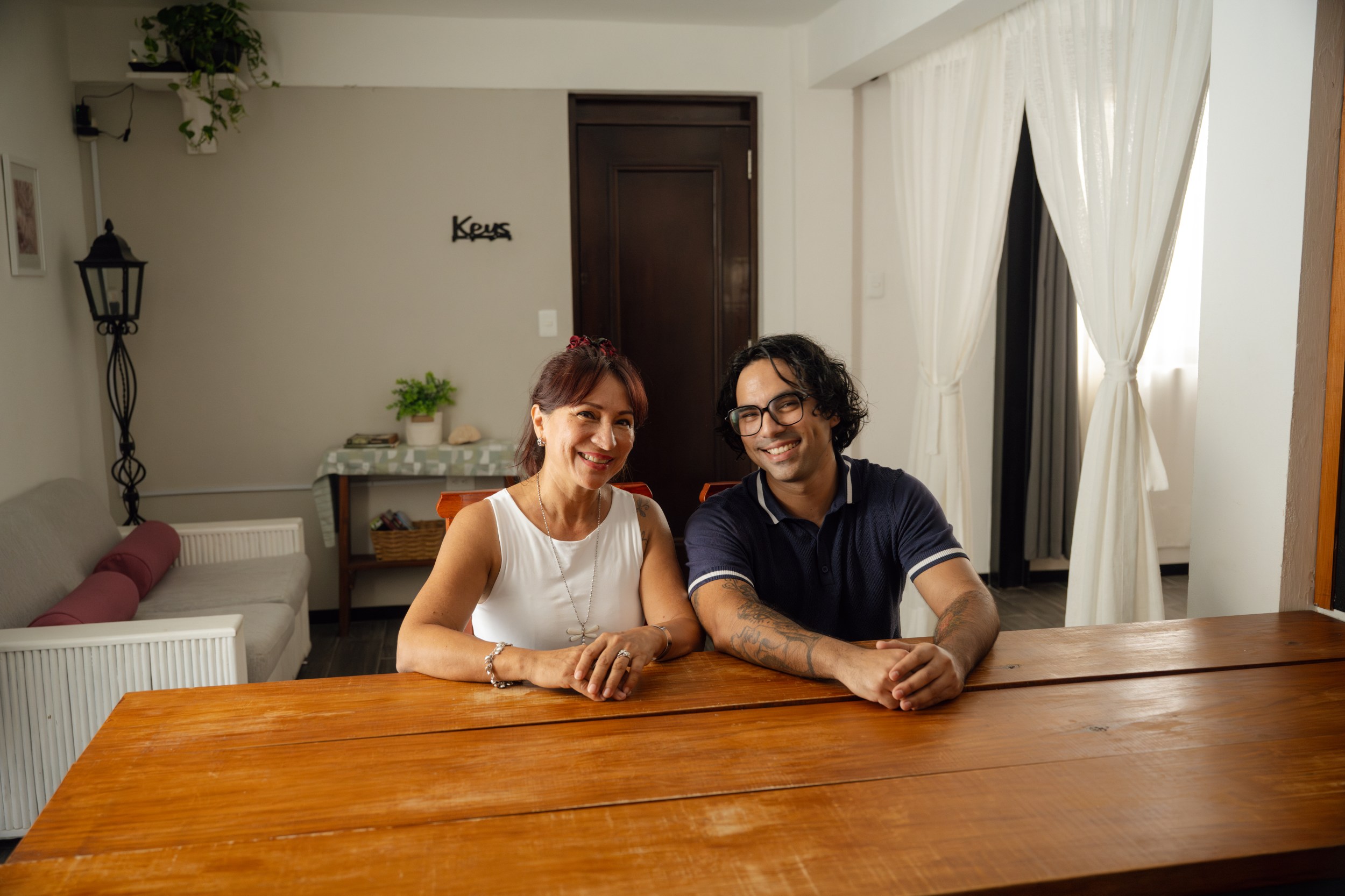 Pareja sentada mirando a la camara y al frente de una mesa de madera