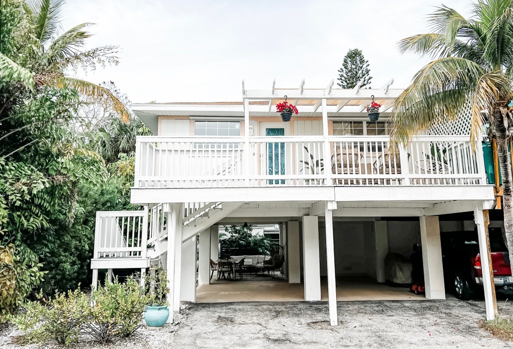 White villa with a front porch surrounded by palm trees.