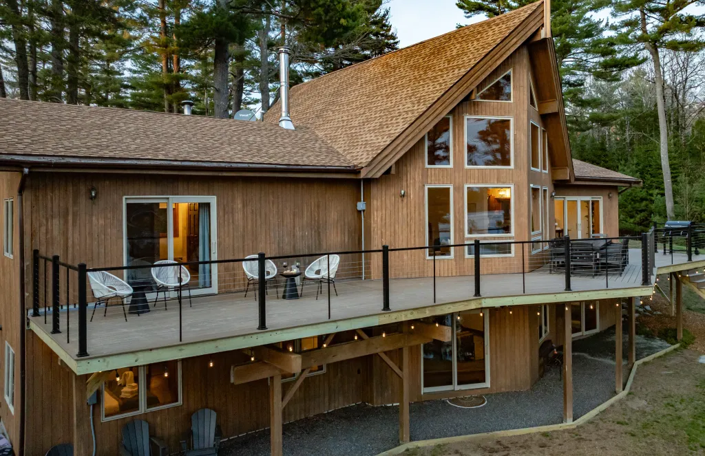 A spacious wooden chalet features expansive windows and a wraparound deck, surrounded by tall pine trees for a tranquil forest escape.