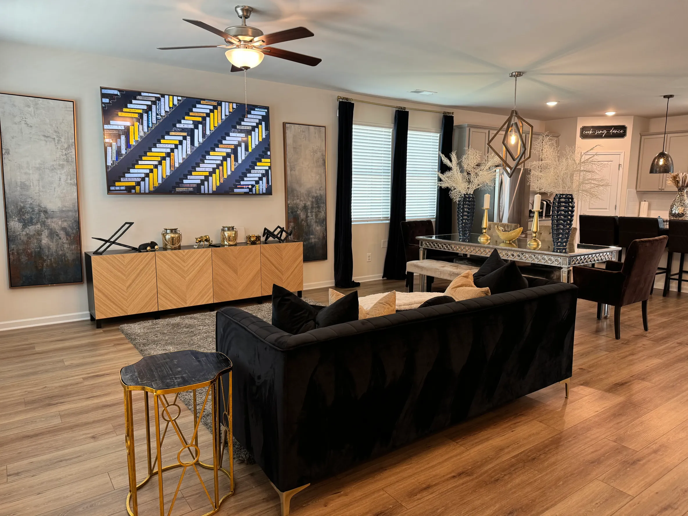 Stylish open-concept living and dining area with modern art, dark velvet sofa, gold accents, and a sleek mirrored table.