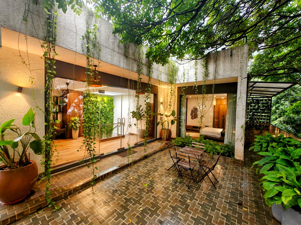 Lush garden patio with abundant greenery, floor-to-ceiling windows, and tranquil outdoor seating adjoining a modern home.