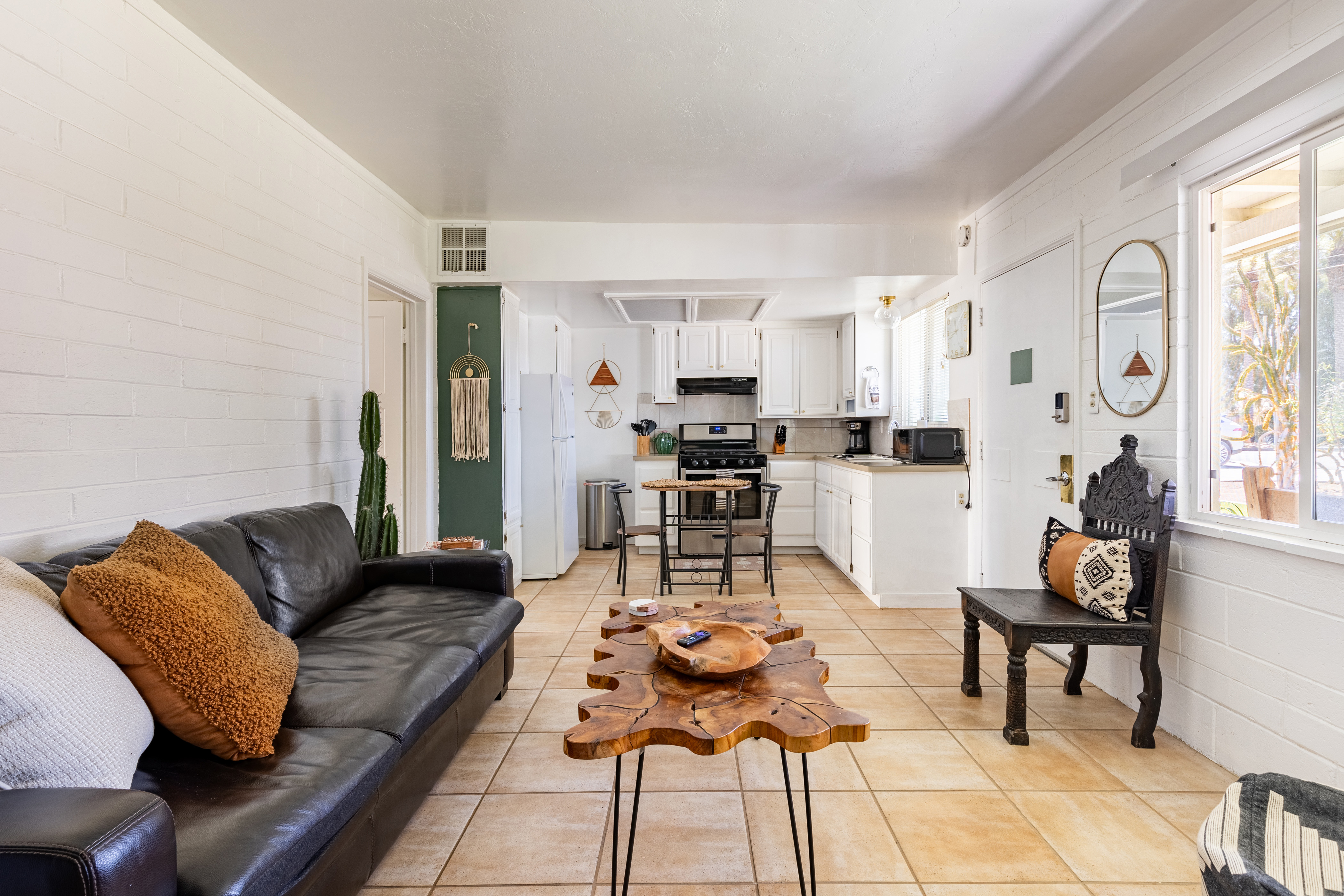 Eclectic living area with a black leather sofa, organic wood coffee table, southwestern accents, and a white kitchen.
