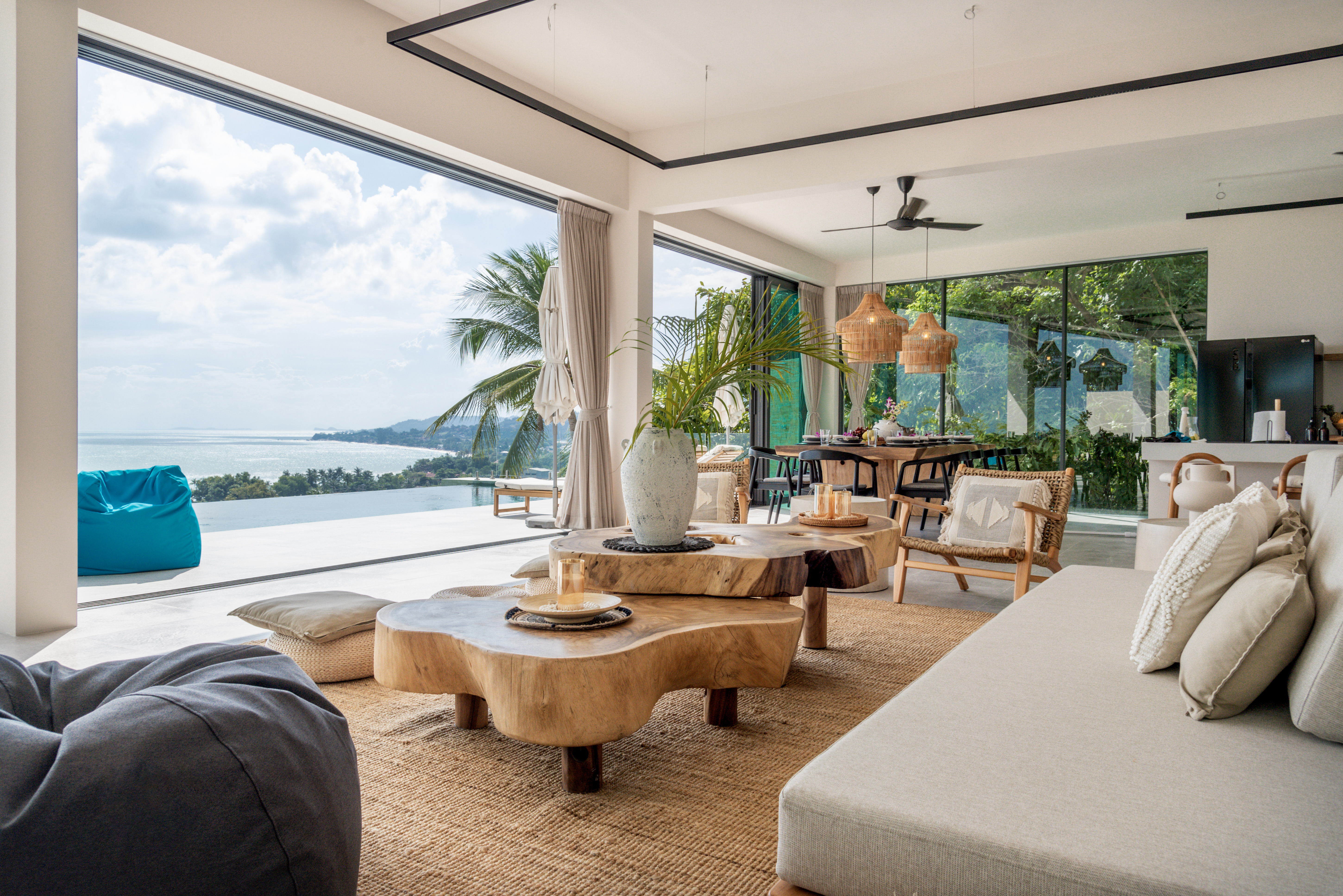 An airy, open-concept living space with organic wood furnishings seamlessly blends into a tropical outdoor terrace overlooking the ocean.