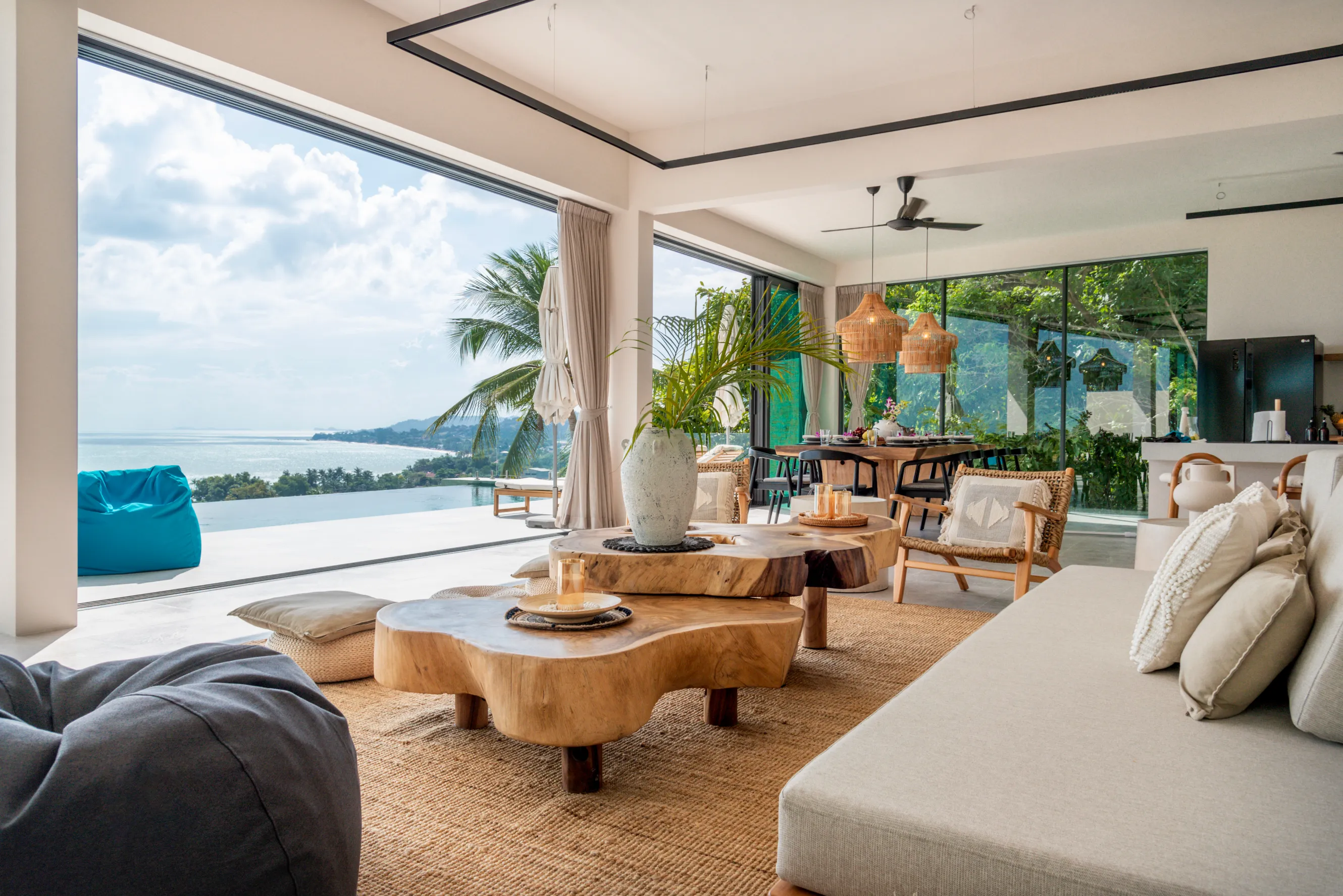 An airy, open-concept living space with organic wood furnishings seamlessly blends into a tropical outdoor terrace overlooking the ocean.