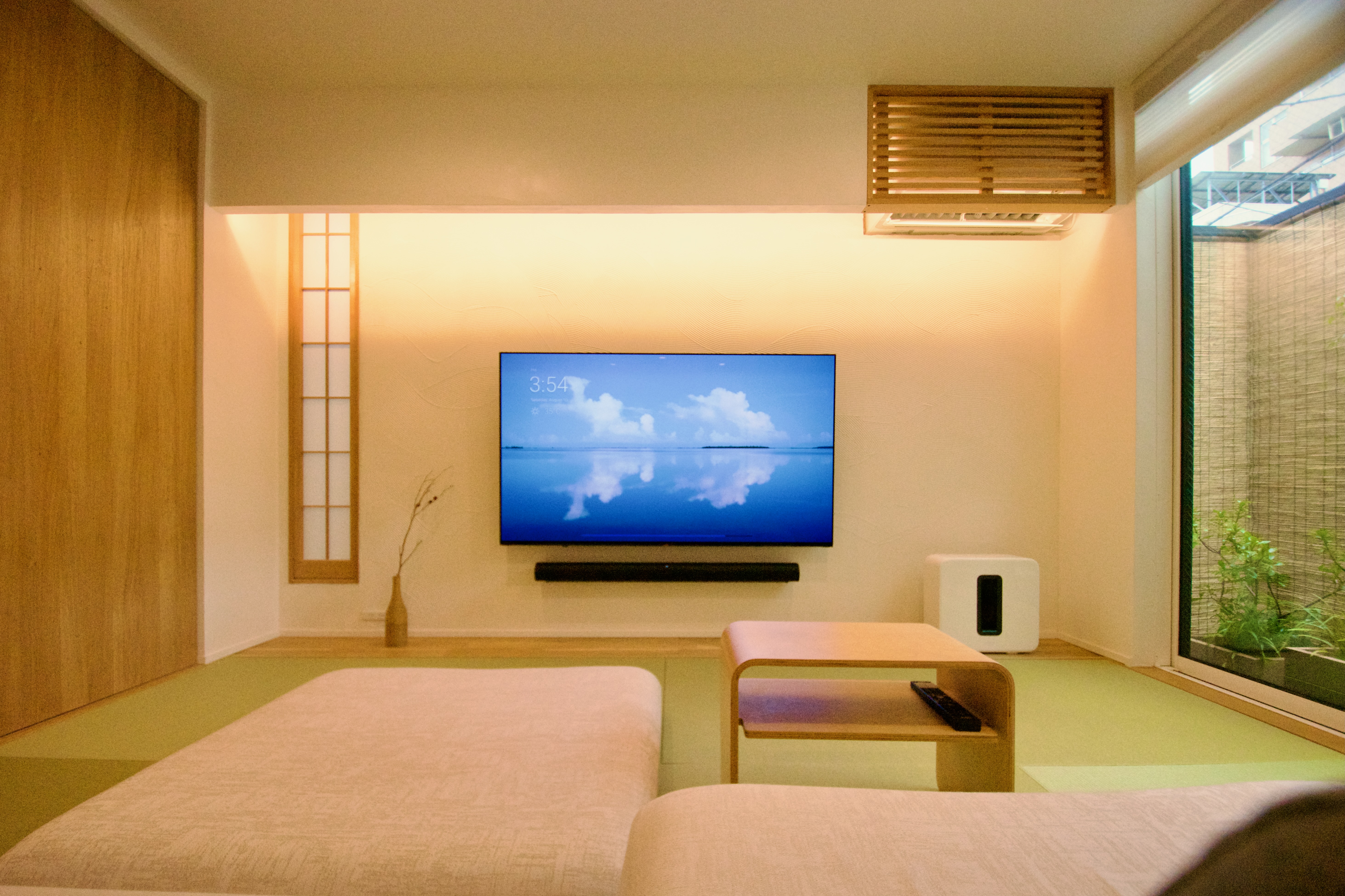 A minimalist living room with Japanese-inspired design elements centers around a wall-mounted television and serene, natural touches.