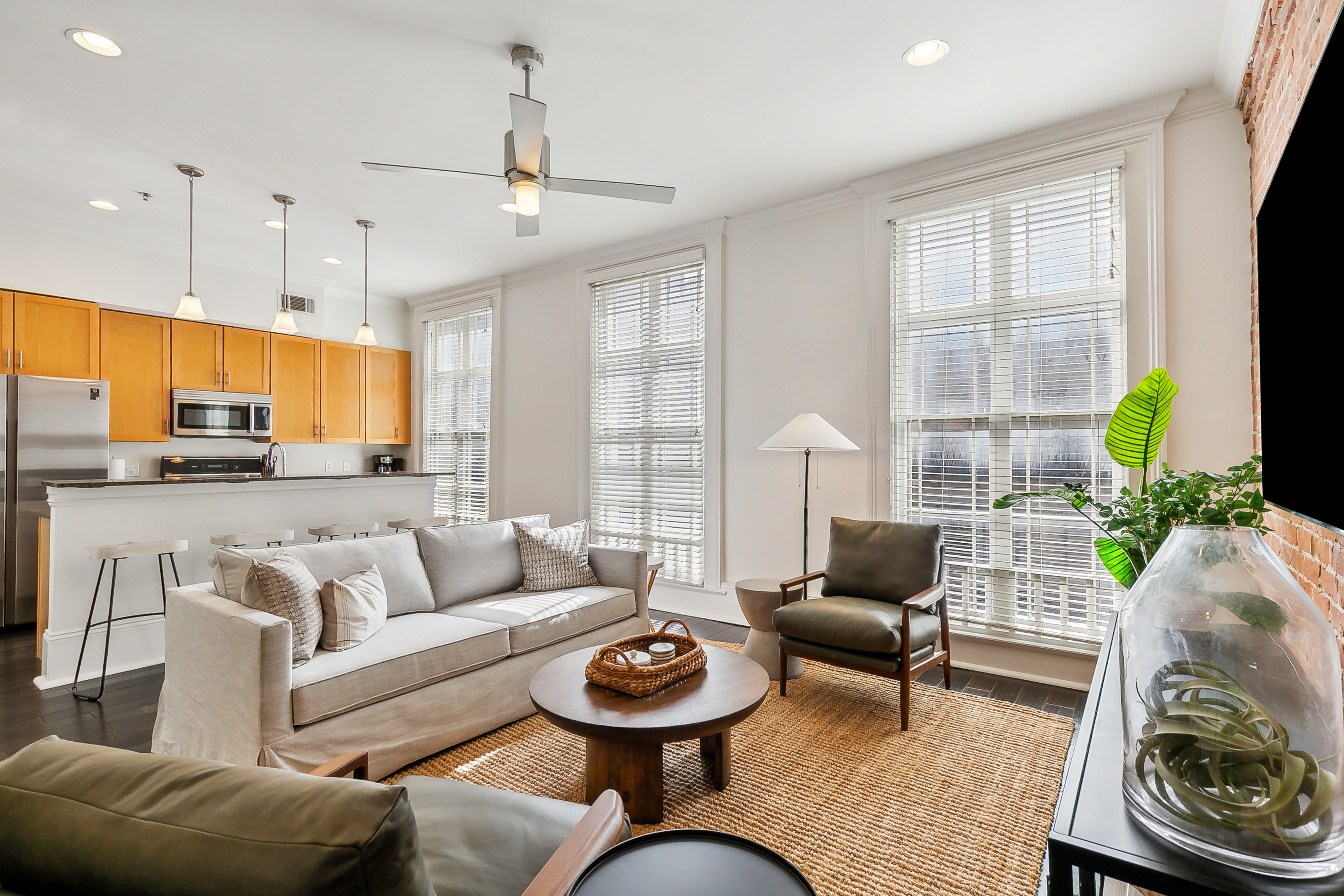 An open-concept living space blends a sleek kitchen with warm wood cabinets and a cozy sitting area, highlighted by natural light and contemporary furnishings.