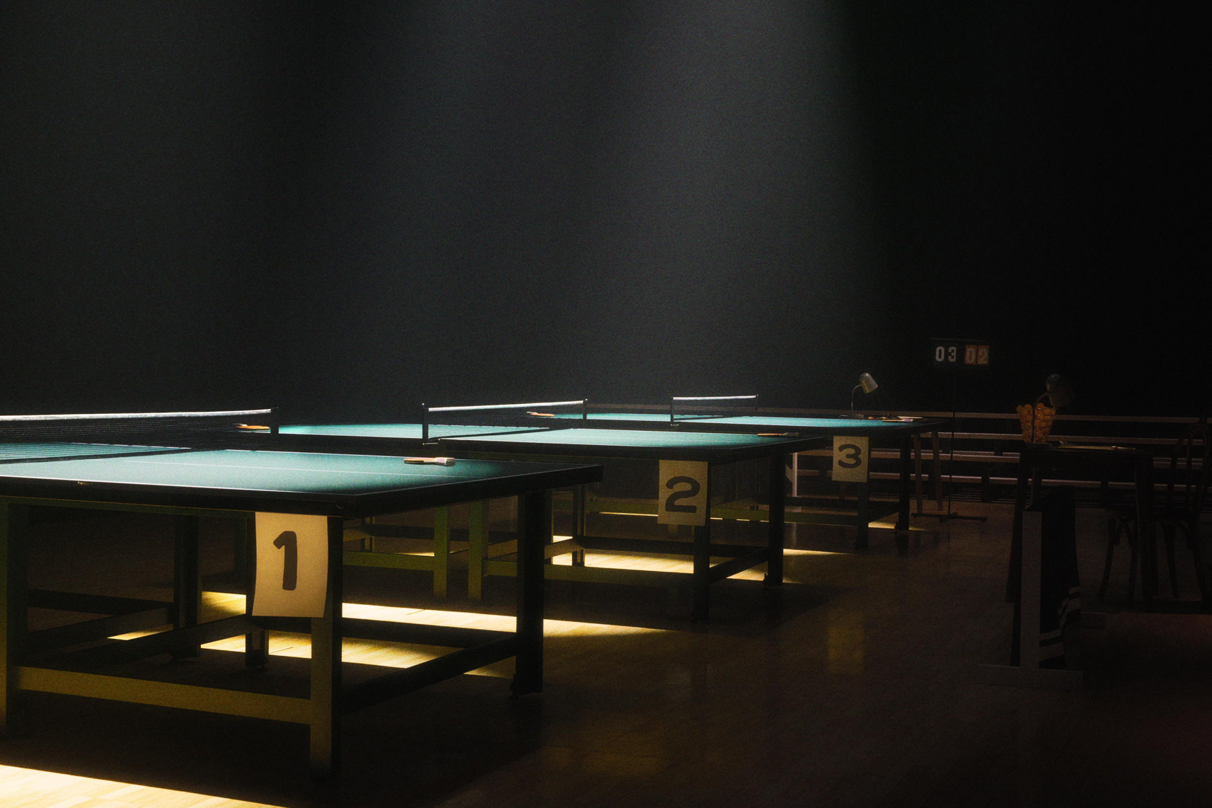 Three table tennis tables in a gym with scoreboard in the back