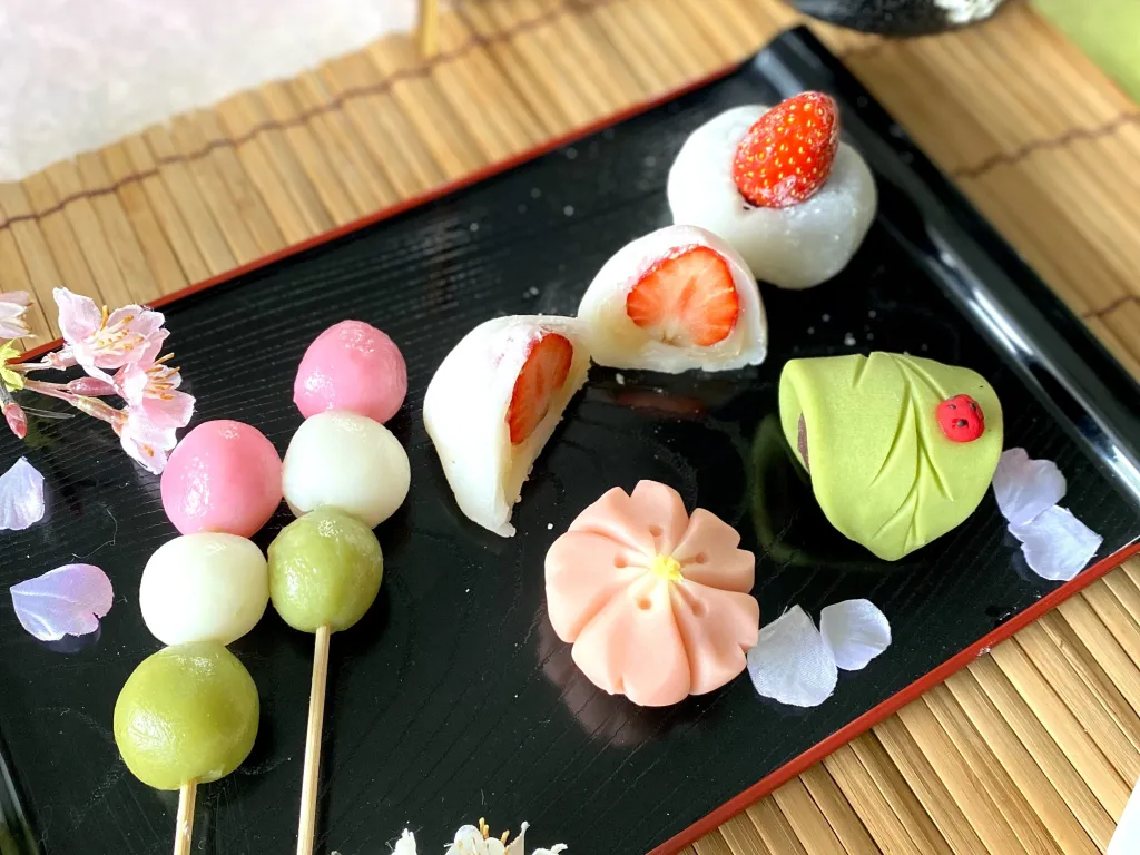 An assortment of mochi shaped in flowers and some with strawberries on top.