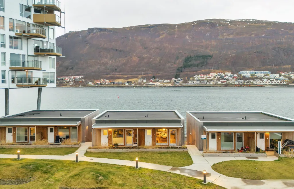 Waterfront modular homes with modern design, set against a scenic mountain backdrop and a calm river.